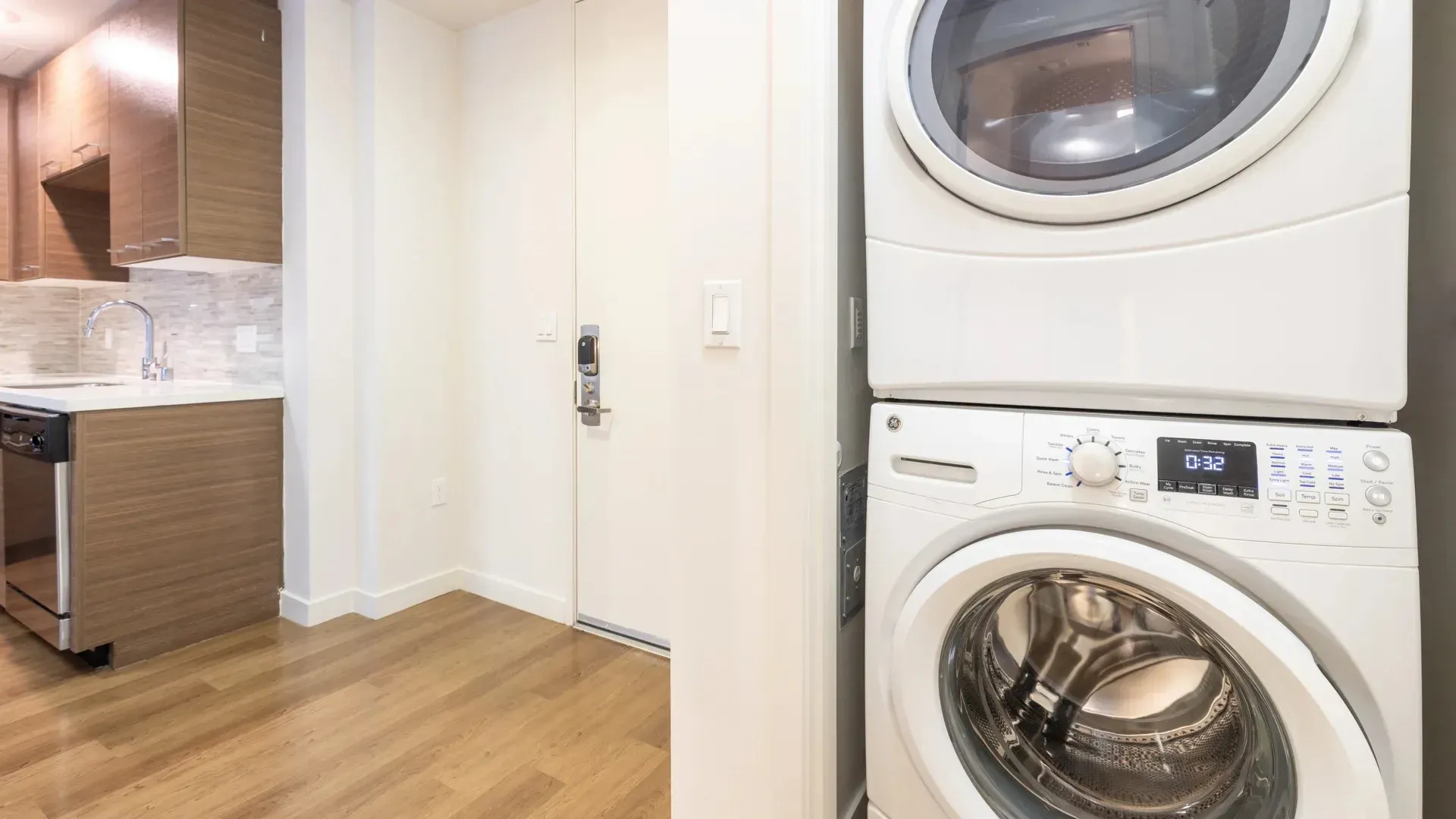 Stackable washer and dryer next to a kitchen area and a door with a smart lock.