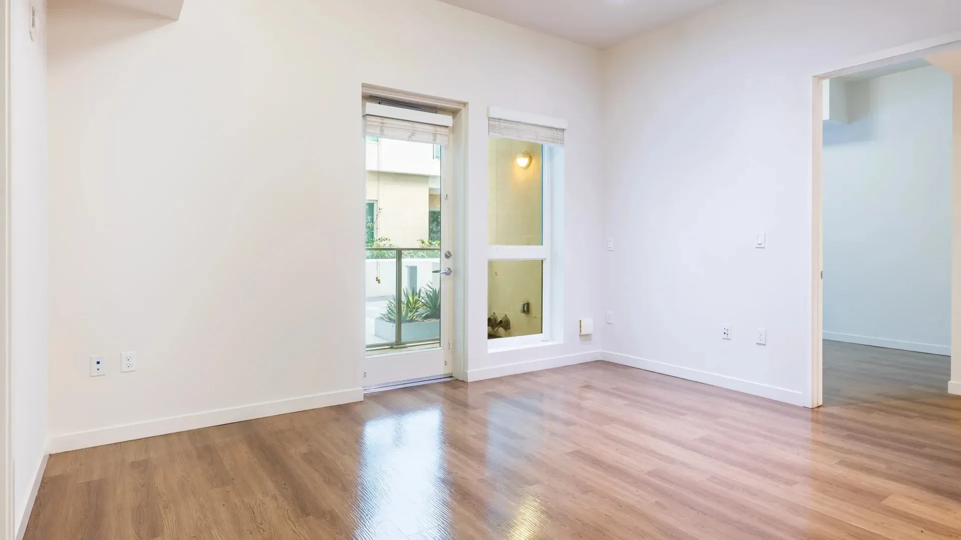 Empty apartment living room with large windows and a glass door leading to a balcony.