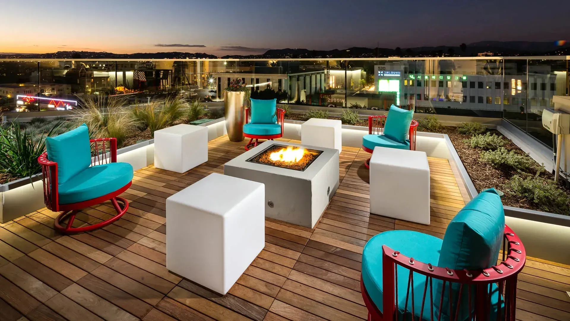 Rooftop lounge area with a fire pit, seating, and city views at dusk.