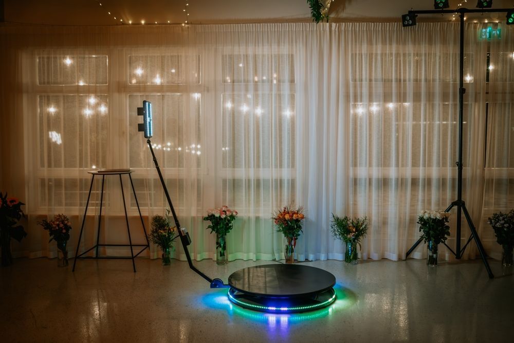 Empty event stage with sheer curtains, tripods, potted plants, and a glowing circular LED platform.