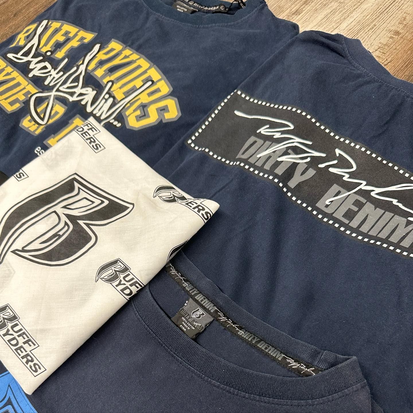 Folded navy and cream graphic T-shirts with bold printed logos and text.