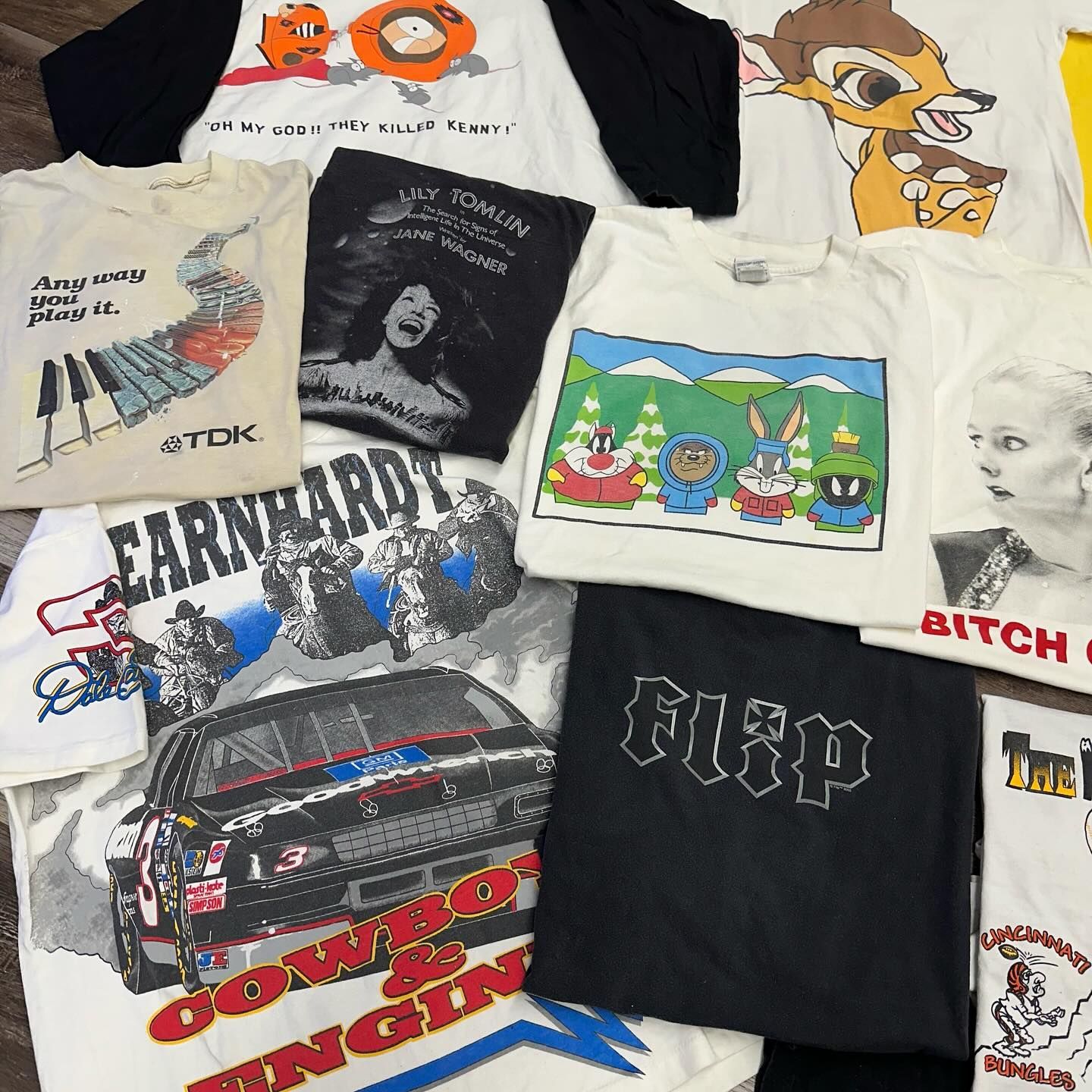 Assorted graphic T-shirts laid out on a surface, featuring cartoon, band, and logo designs.