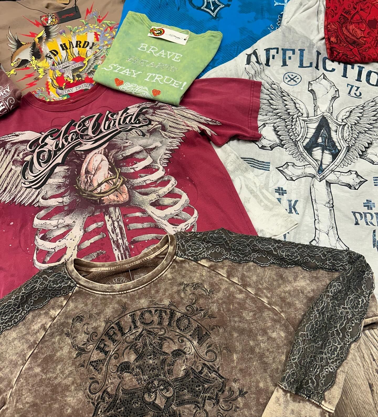 Assorted graphic T-shirts laid out on a bed, including red, white, green, and brown designs.