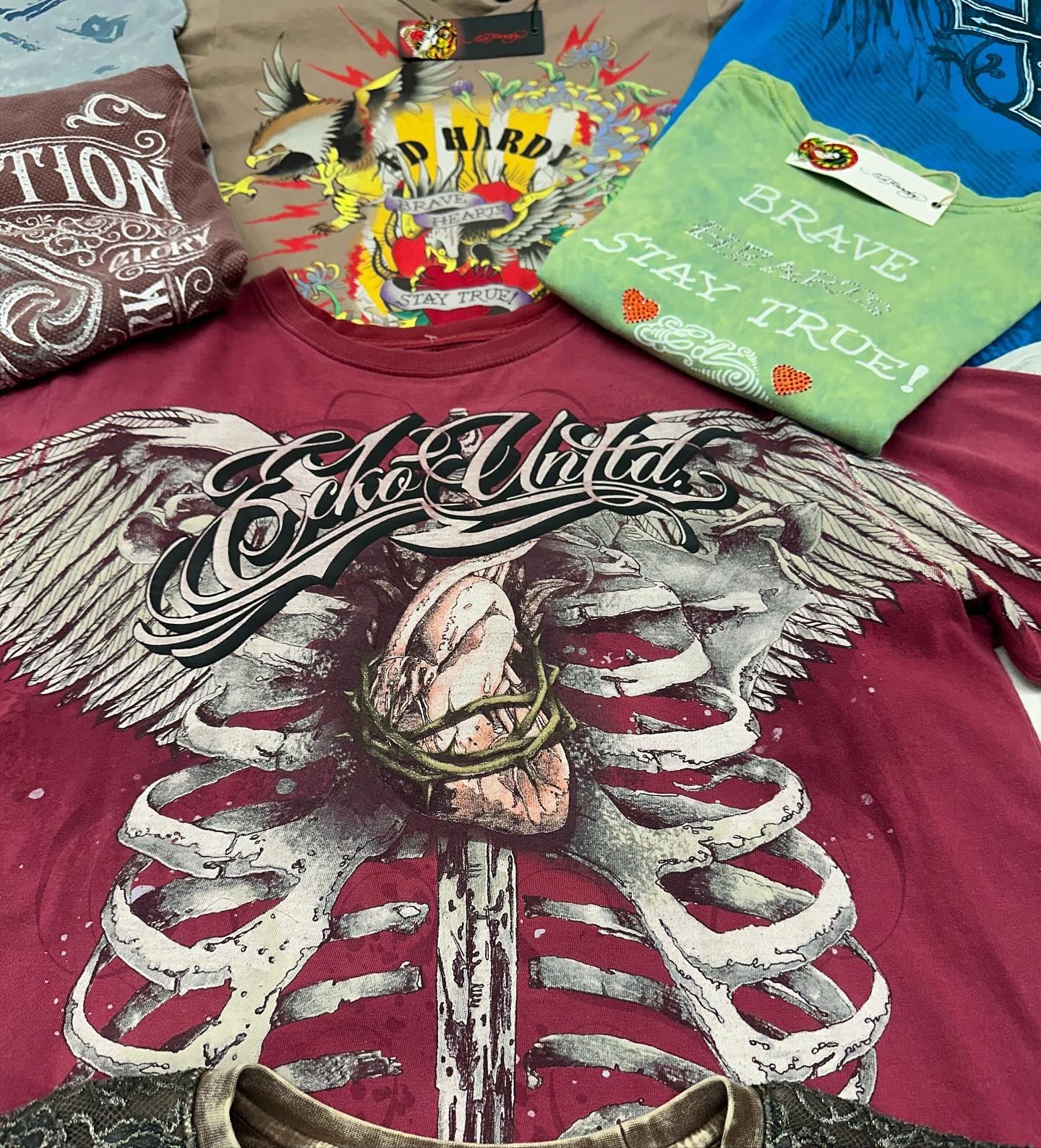 Three folded graphic T-shirts in maroon, green, and brown with bold printed designs on a bed