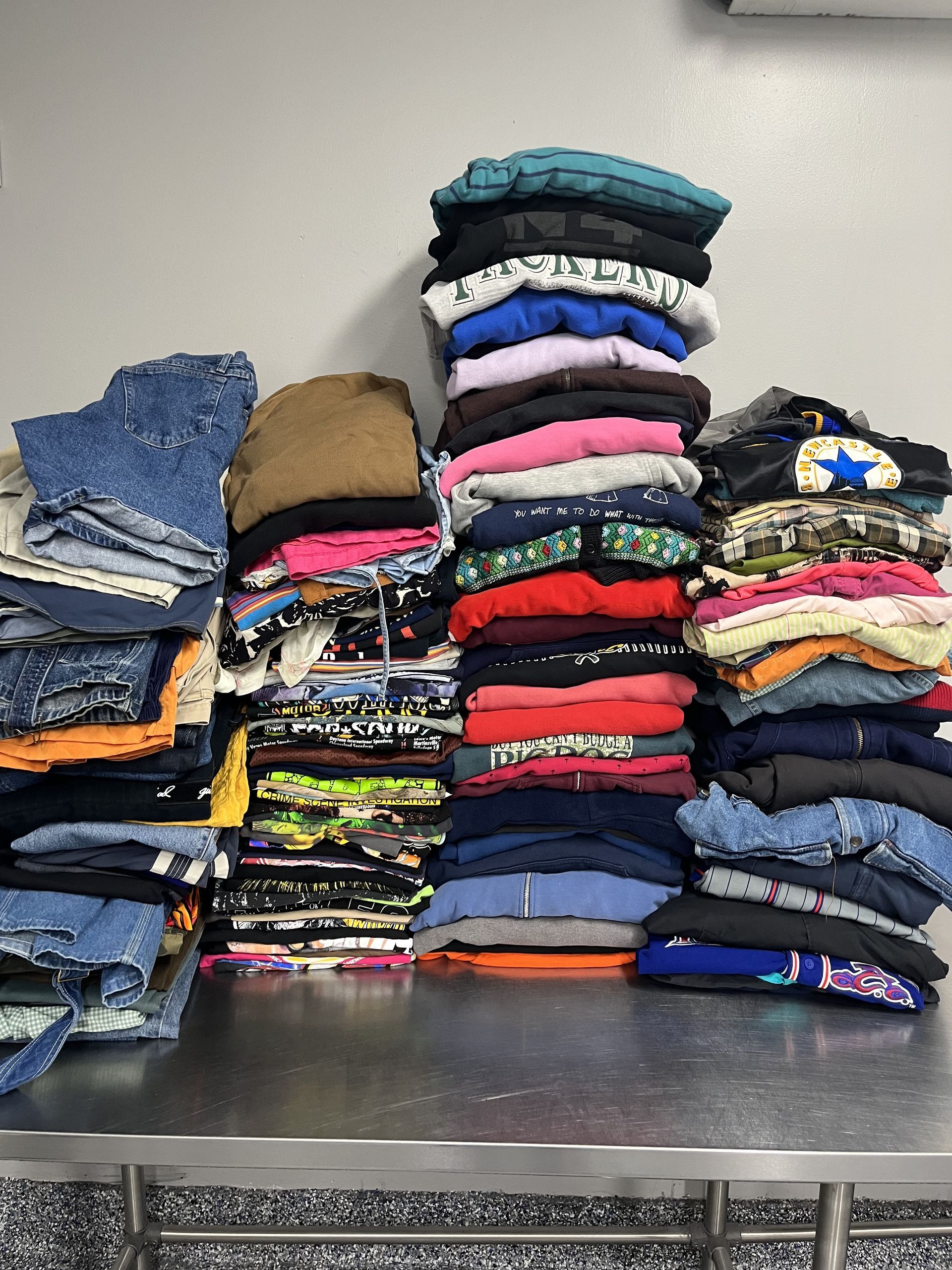 Stacks of folded clothes in assorted colors piled on a metal table.