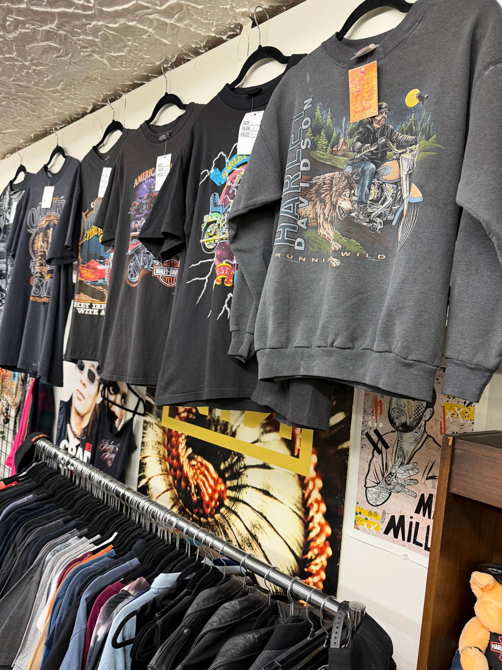 Black graphic T-shirts hanging on a rack in a clothing shop, with a yellow artwork print below.
