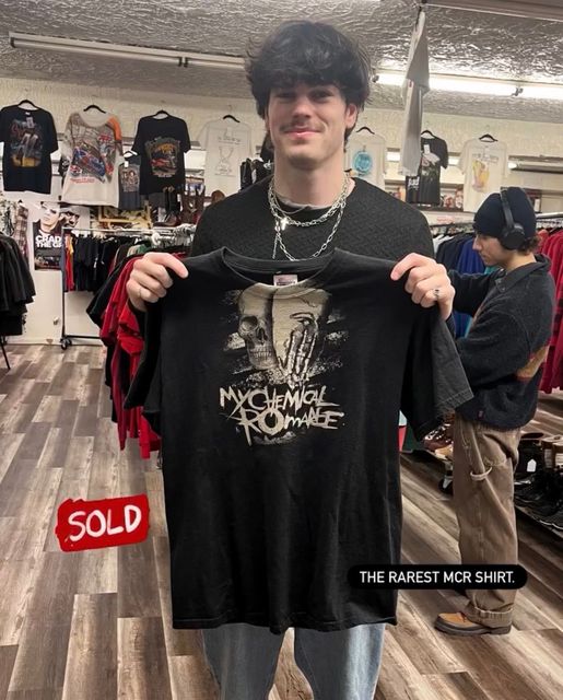 Man holding a black My Chemical Romance T-shirt in a thrift store, with a “SOLD” label.