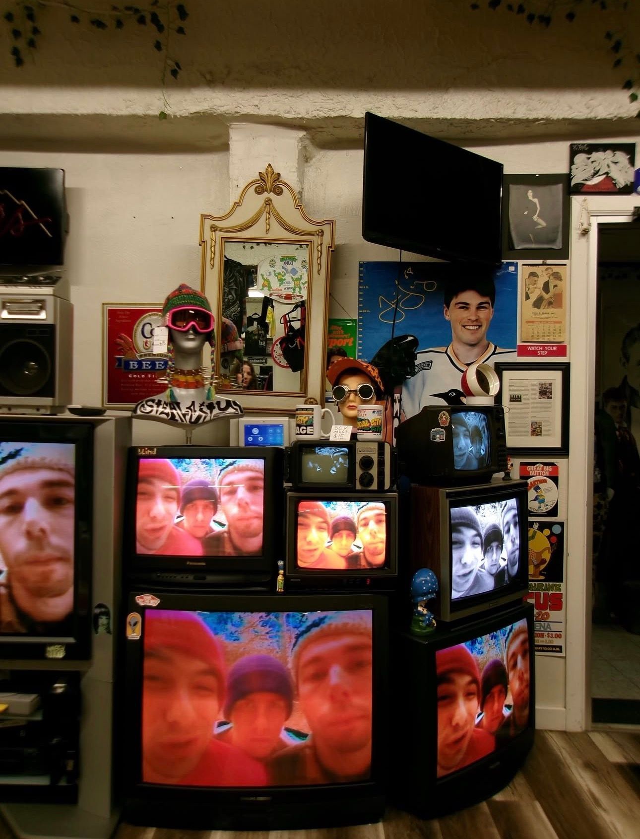 A room packed with multiple TVs showing faces, with shelves of collectibles and framed pictures behind them