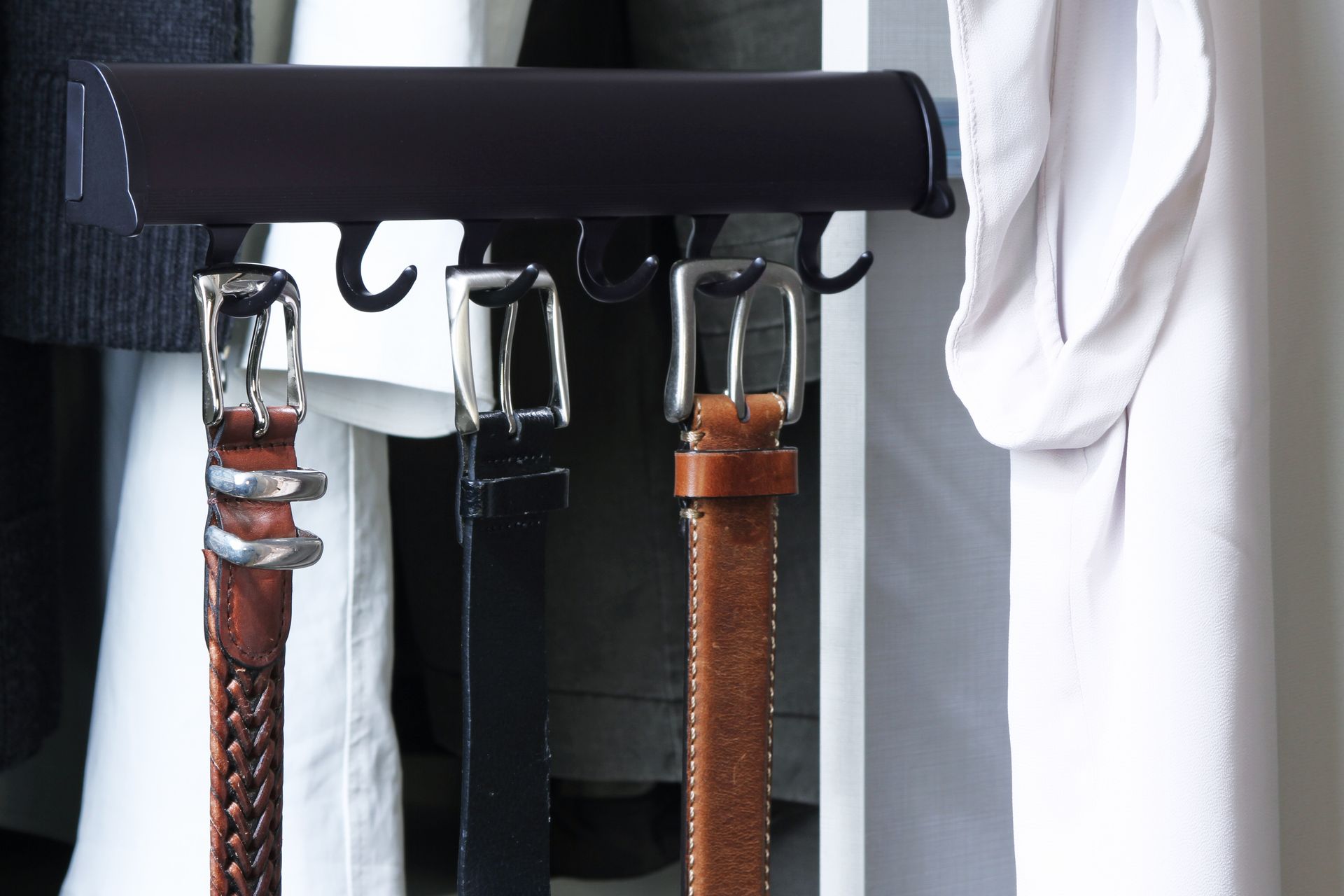 Belts hanging on a rack, including brown, black, and white belts with silver buckles