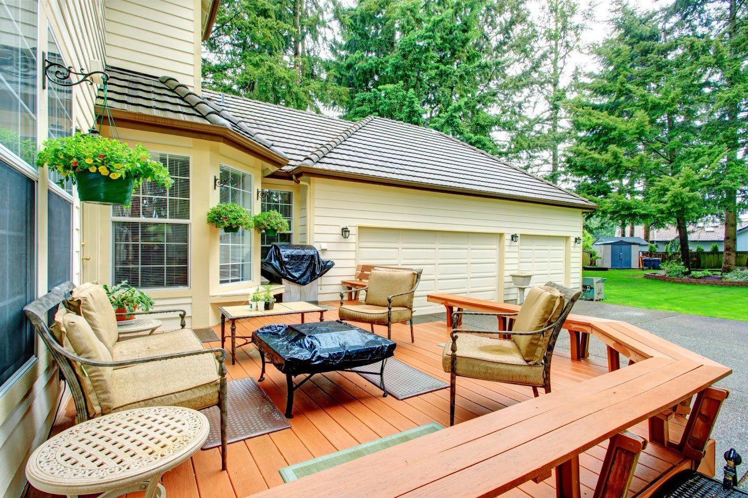 Backyard deck with wicker chairs, black fire pit, and potted plants beside a house