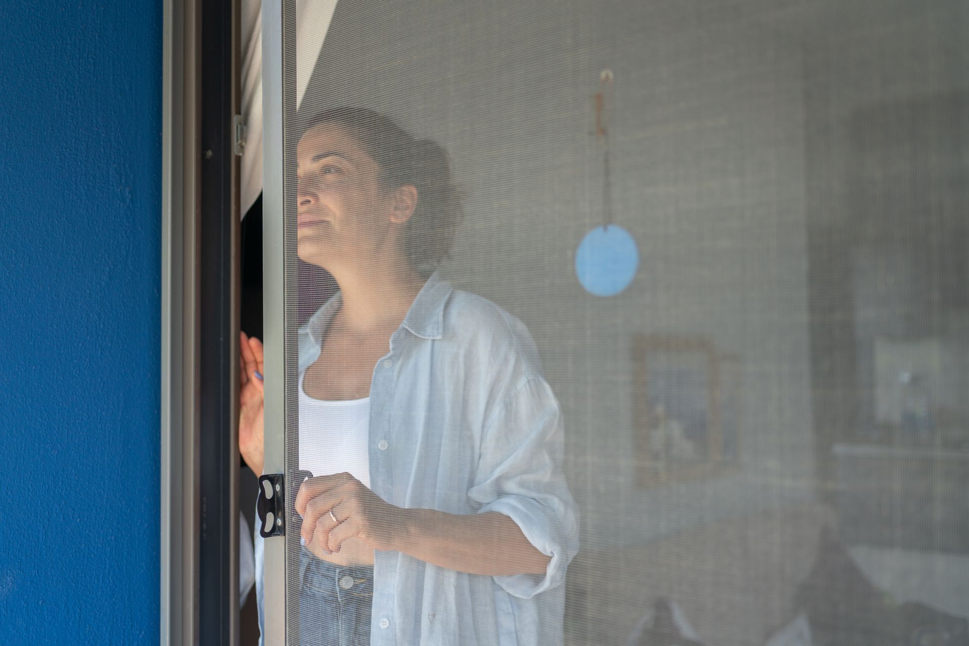 Person opening a screen door, smiling in a doorway with a blue wall visible on the left
