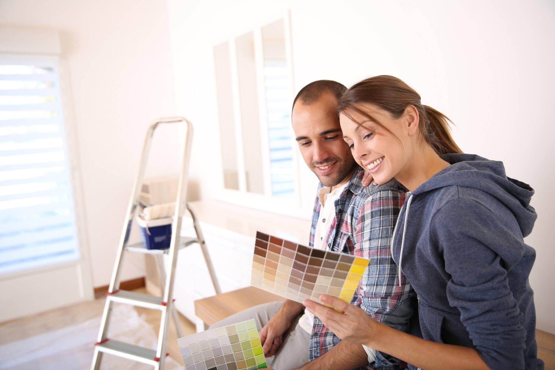 Two people reviewing paint swatches in a bright room with a ladder and paint supplies.
