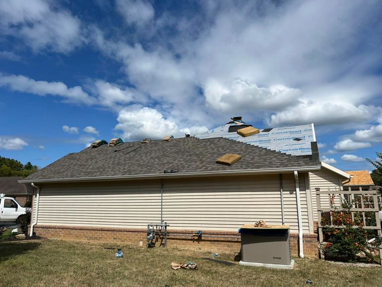 House roof severely damaged with missing shingles under a cloudy blue sky