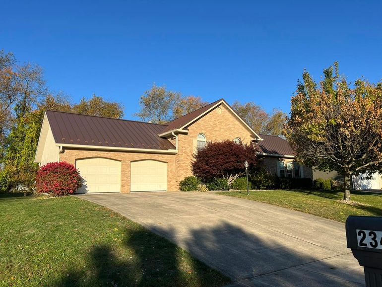 Suburban house with two-car garage, driveway, and autumn trees under a clear blue sky