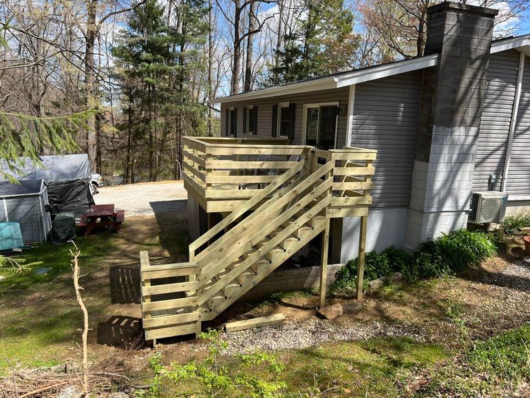 Wooden ramp and stairs leading to a house porch in a wooded yard