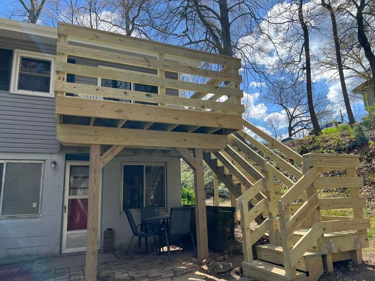 Wooden deck and staircase addition on a house, with railings and a shaded patio below.