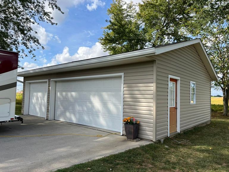 Detached beige garage with white doors and a side entry door beside a driveway