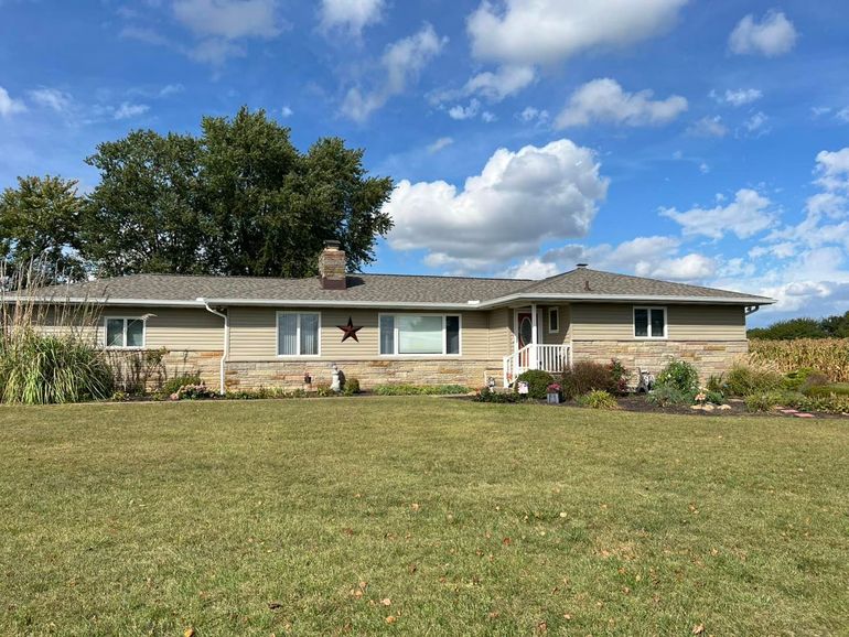 Single-story beige house with a large front lawn under a blue sky with clouds