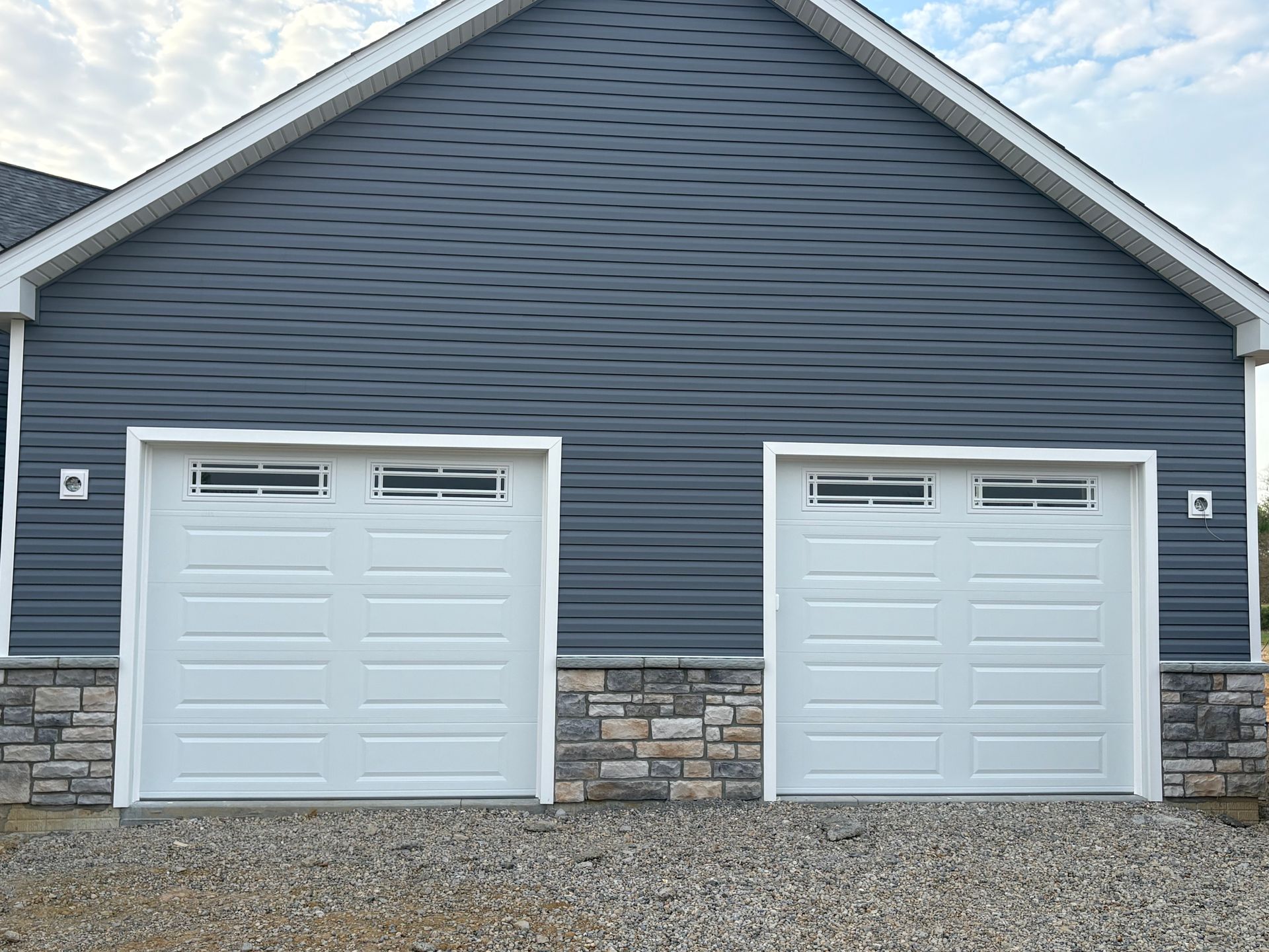 Blue house exterior with two white garage doors and stone base trim
