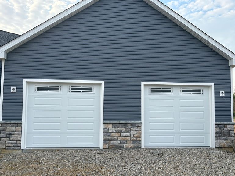 Two white garage doors on a blue house with stone siding