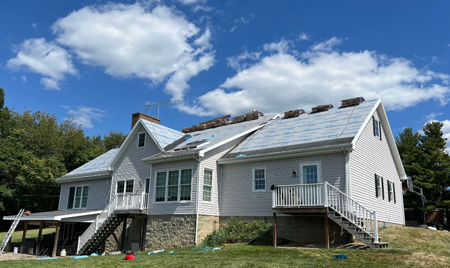 A house undergoing roof replacement, with roofing materials and underlayment visible on the roof.