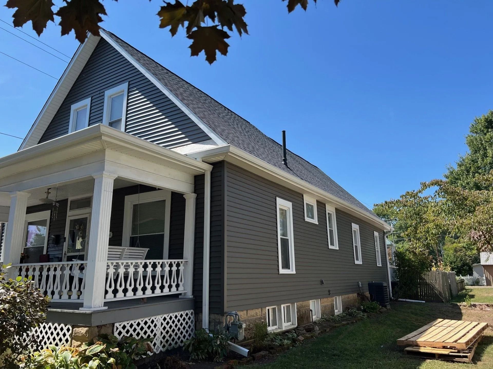 Gray house with new shingle roof and a white-railed front porch.