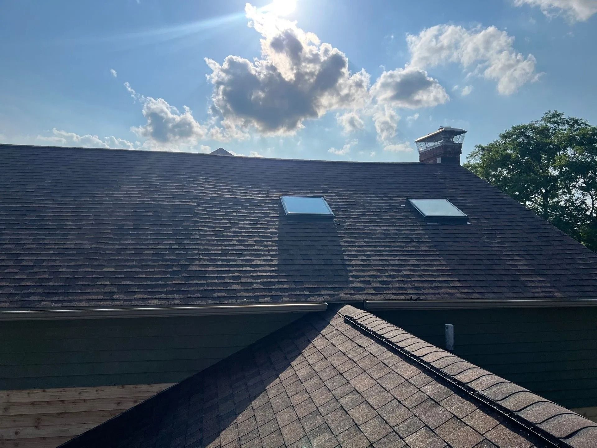Asphalt shingle roof with two skylights and a brick chimney.