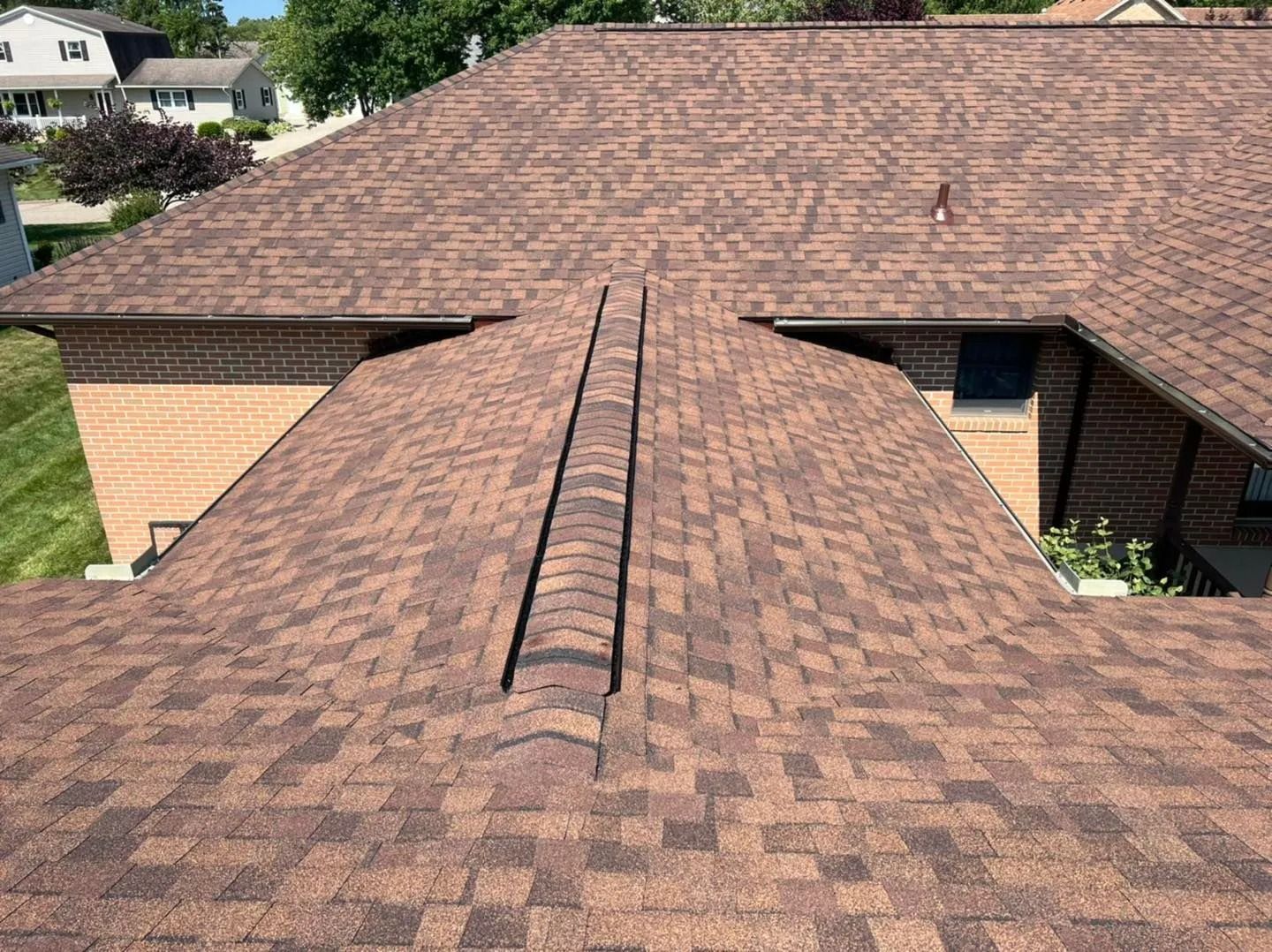 Brown asphalt shingle roof with a ridge vent above a brick home.