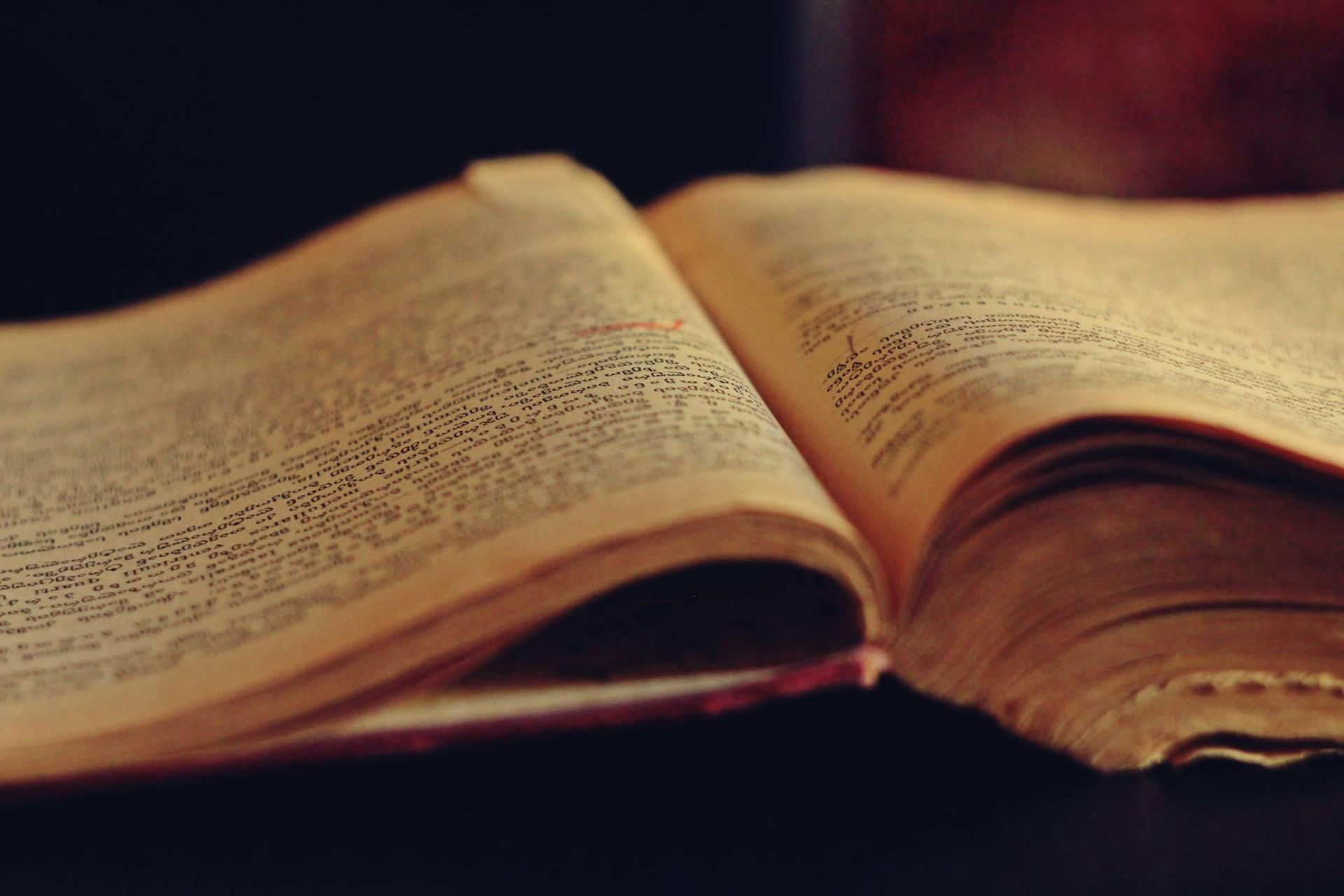 An open book with yellowed pages lying on a dark surface in warm, dim light