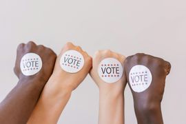Four raised fists with circular “VOTE” stickers against a light background