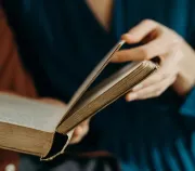 Hand turning the page of an open hardcover book, with a blurred dark background