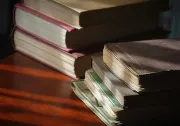 Stacked books on a wooden table, lit by warm sunlight.