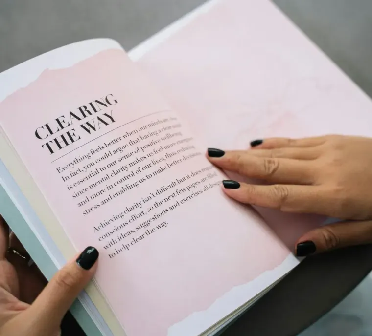 Hands turning pages of a pastel book with a pale pink title page reading “Clearing the Way”