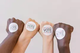 Four raised fists with circular “VOTE” stickers against a light background