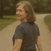 Woman in a dark gray shirt turns back on a winding path, smiling in a wooded park.