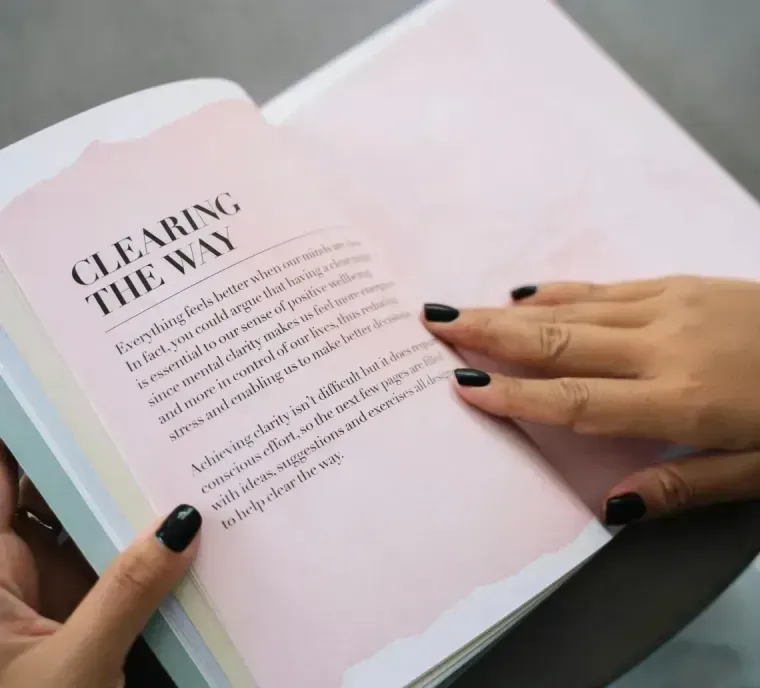 Hands turning pages of a pastel book with a pale pink title page reading “Clearing the Way”