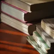 Stacked books on a wooden table, lit by warm sunlight.