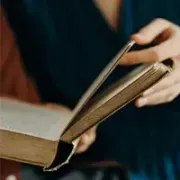 Hand turning the page of an open hardcover book, with a blurred dark background
