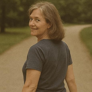 Woman in a dark gray shirt turns back on a winding path, smiling in a wooded park.