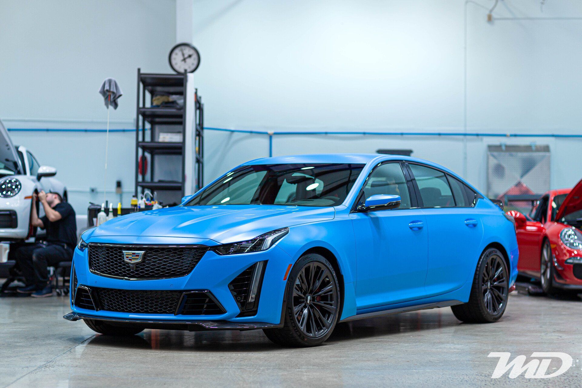 A blue car is parked in a garage next to a red car.