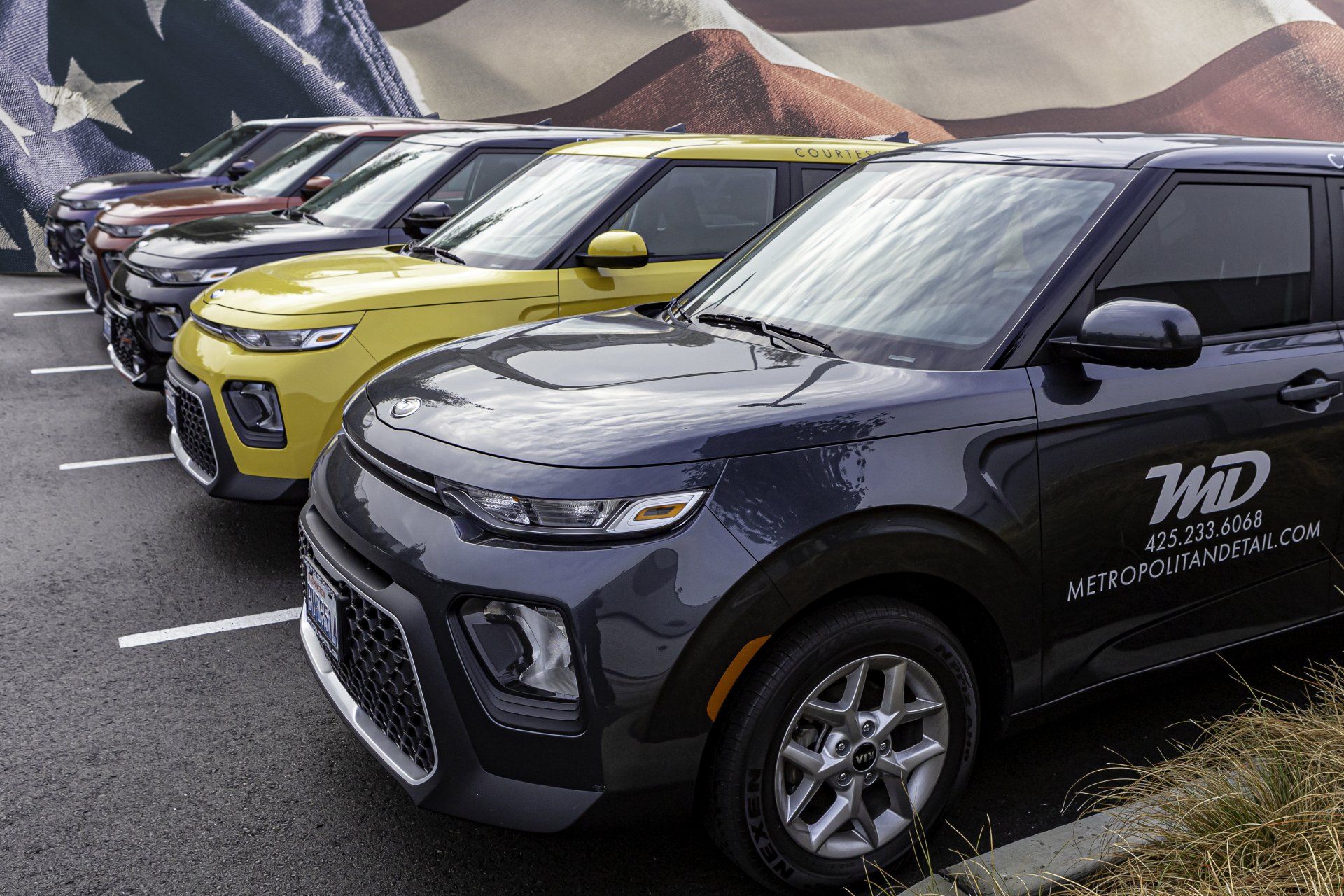 A row of cars are parked in a parking lot in front of an american flag.
