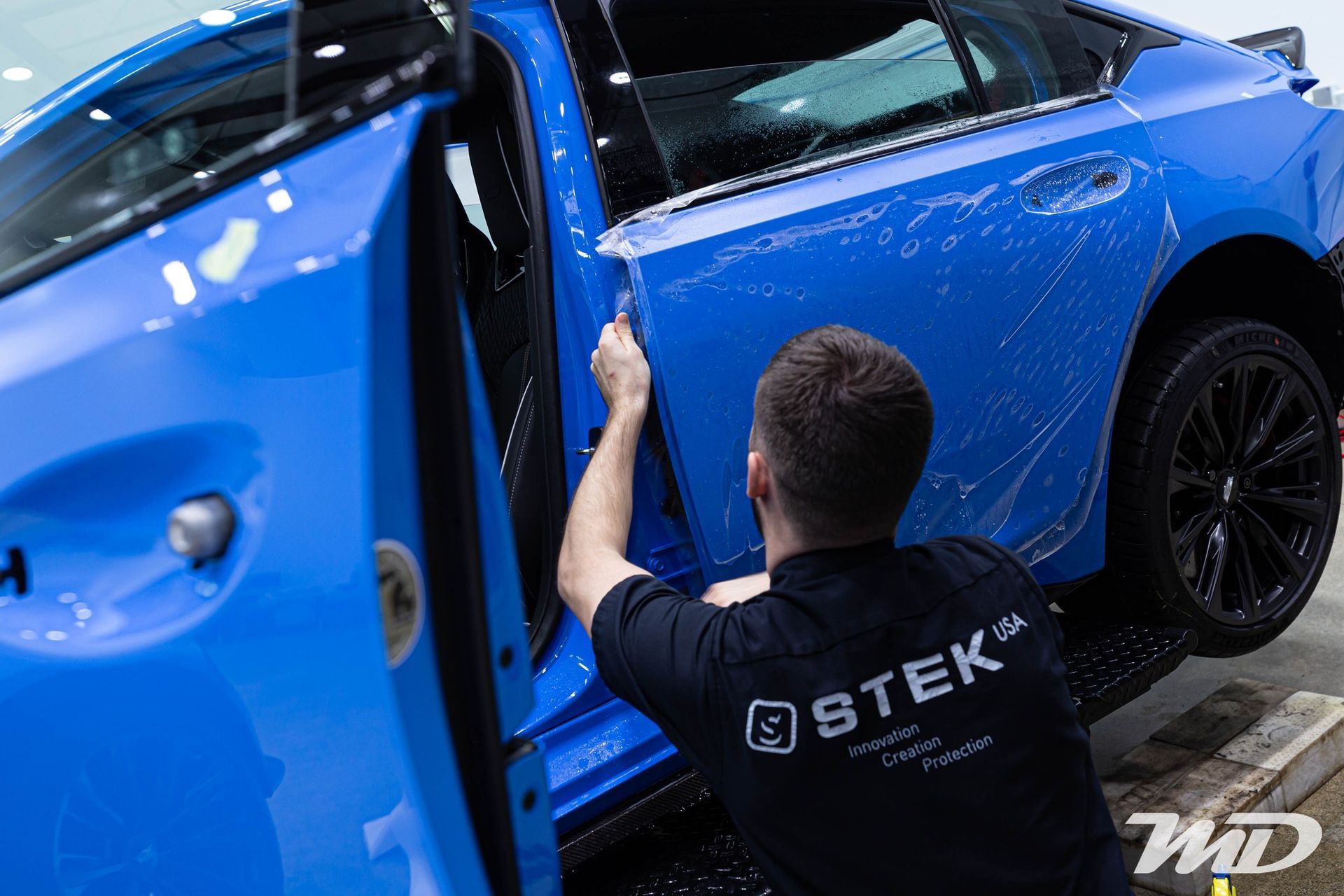 A man is wrapping a blue car with a protective film.