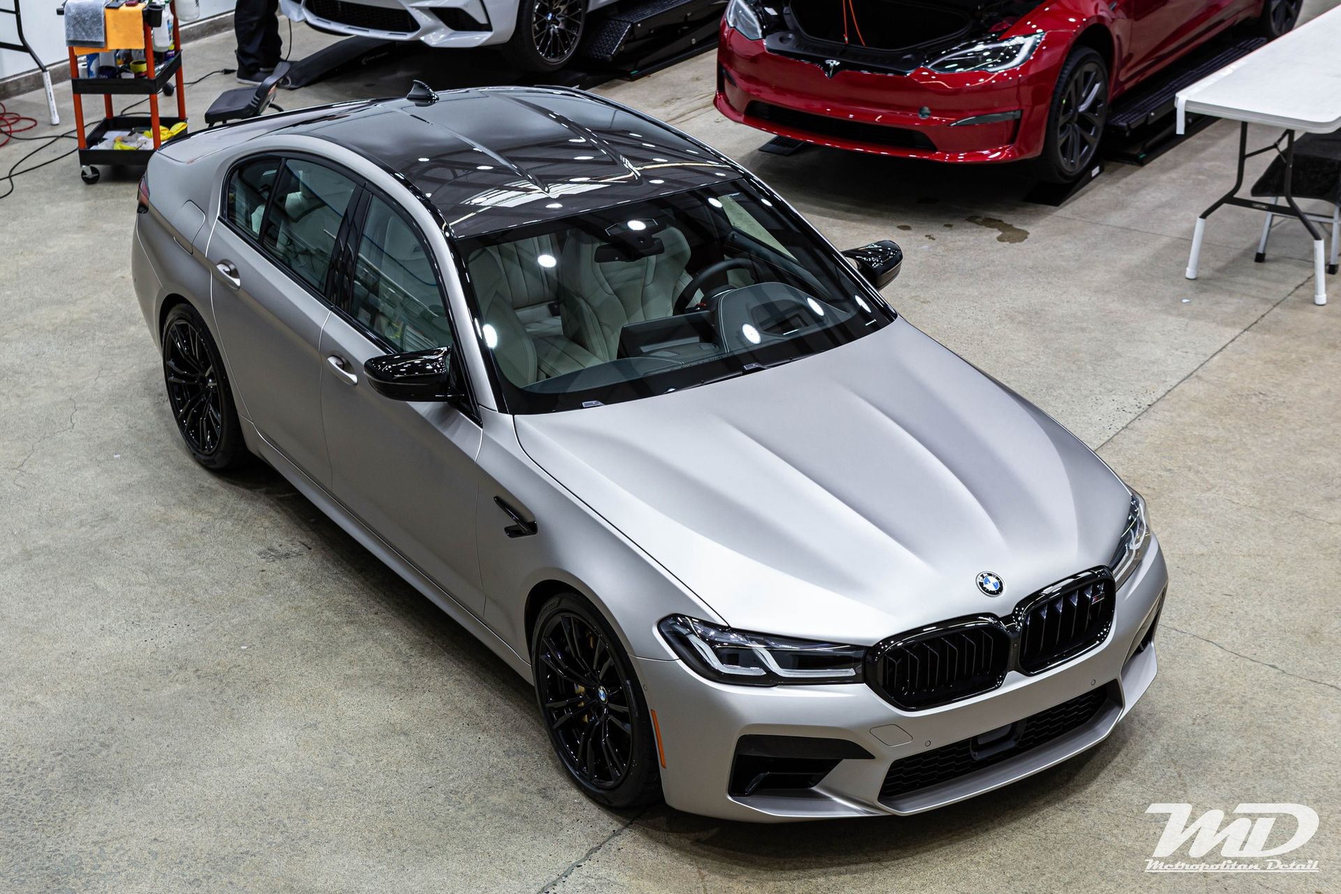 A silver bmw m5 is parked in a garage next to other cars.