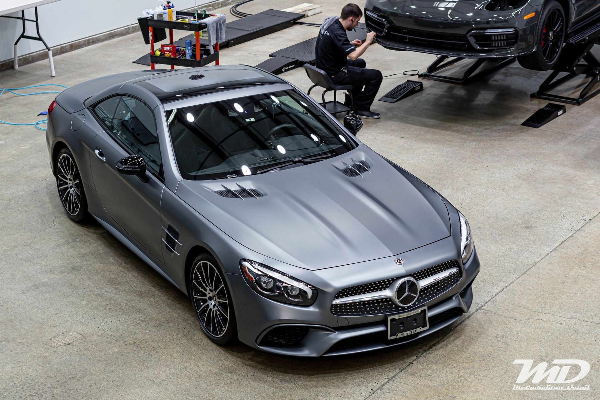 A man is sitting on a chair next to a mercedes sl63 amg convertible in a garage.