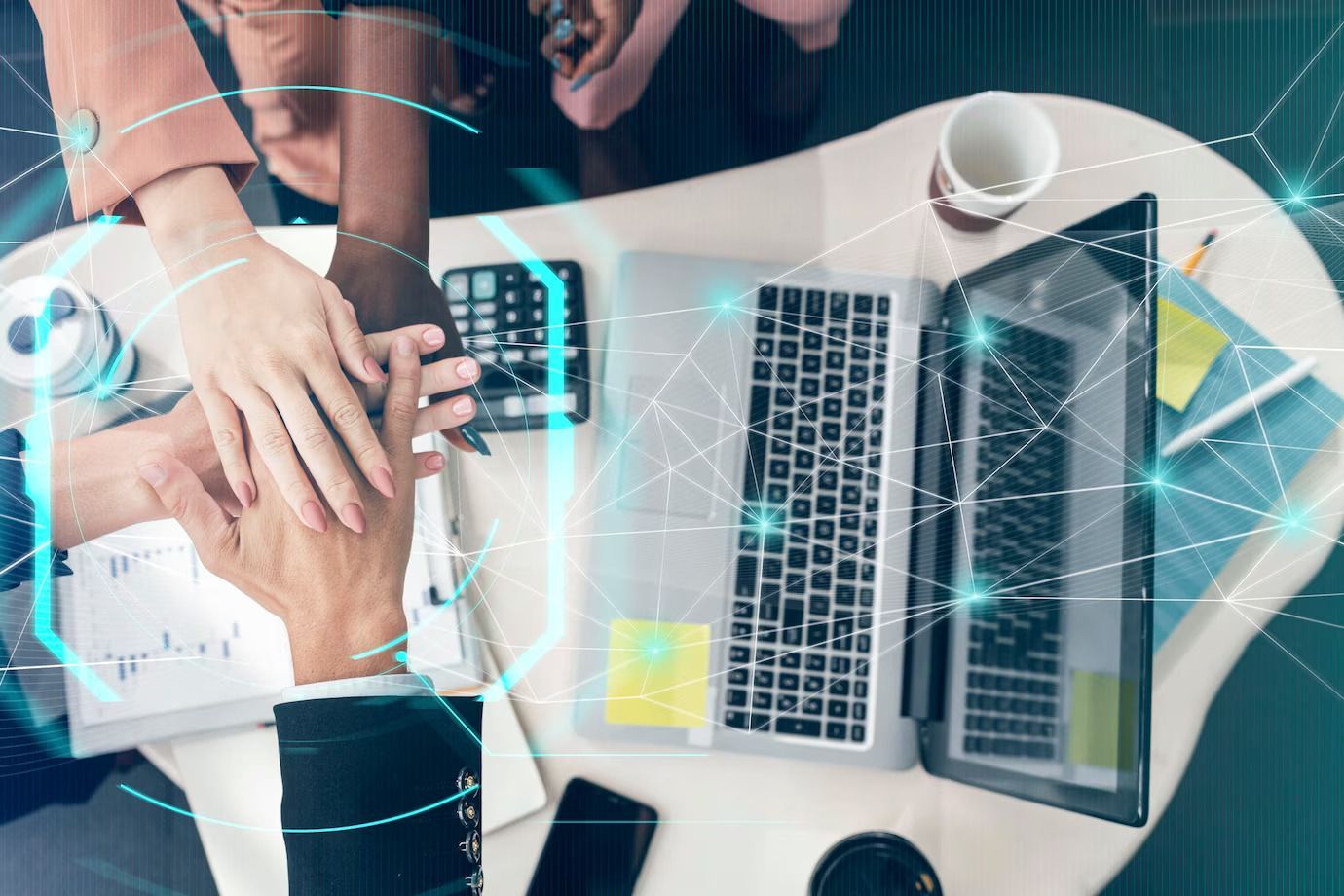 A group of people are sitting at a table with a laptop and putting their hands together.