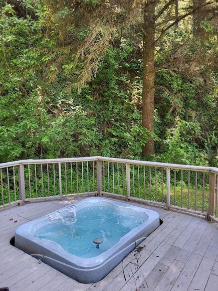 Wooden deck with a small hot tub overlooking a lush green forest.