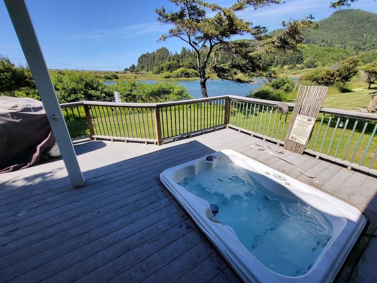 Hot tub on a wooden deck overlooking a blue lake and green hills under a clear sky