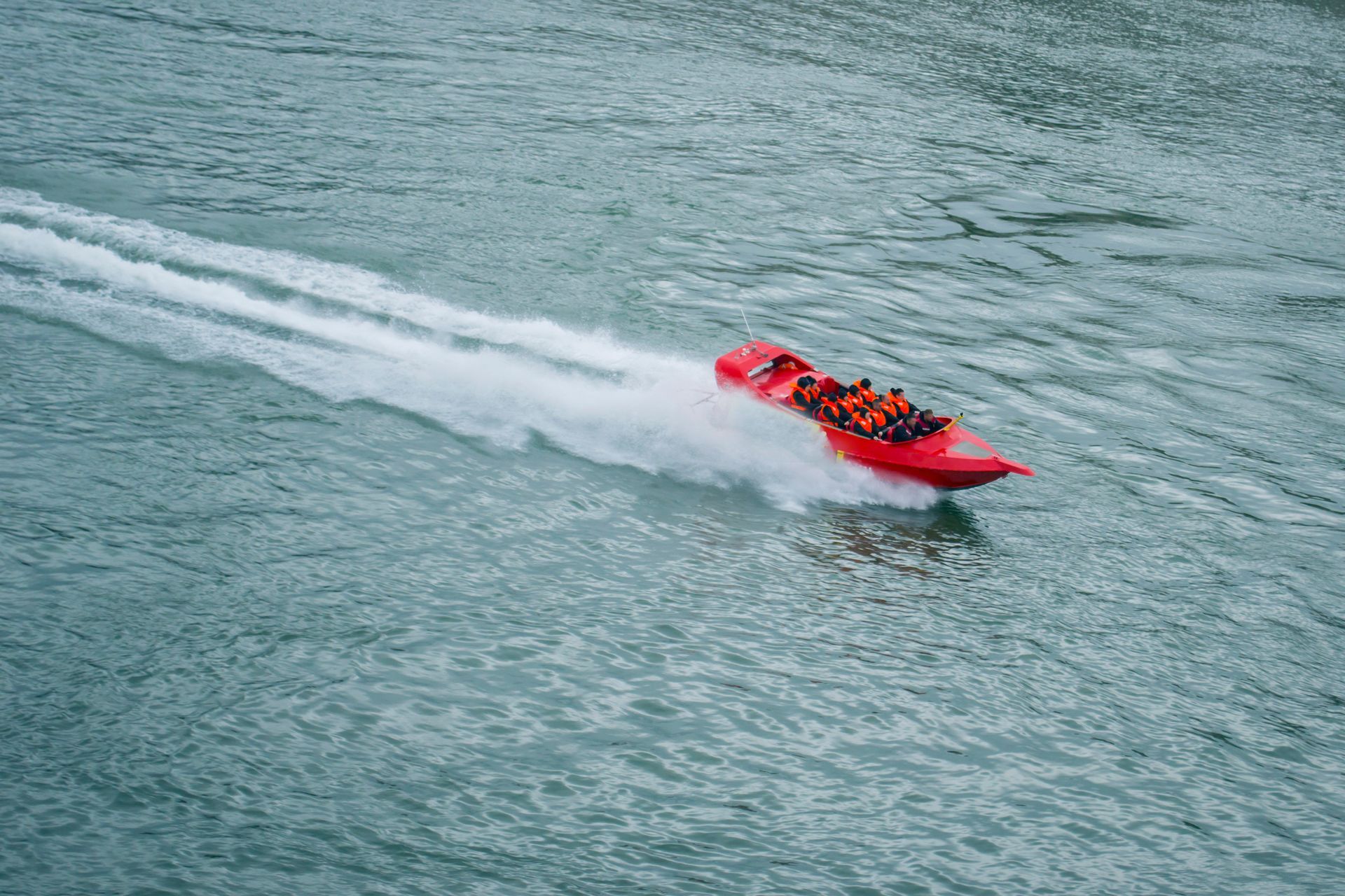 Red speedboat racing across choppy water, leaving a white wake behind it.