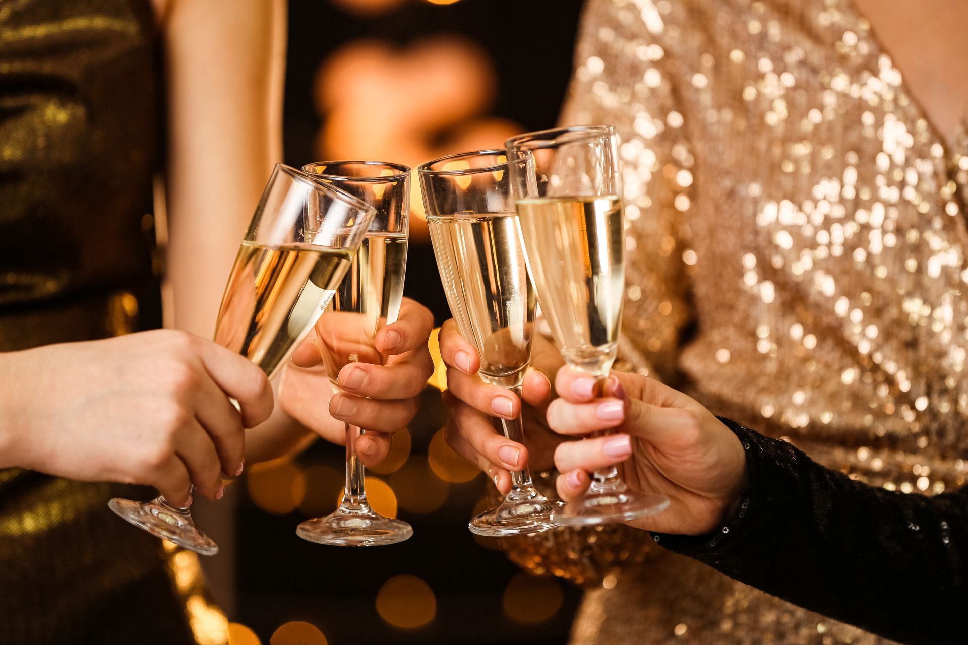 Hands raising champagne flutes at a festive party, with gold sequined clothing and warm lights.