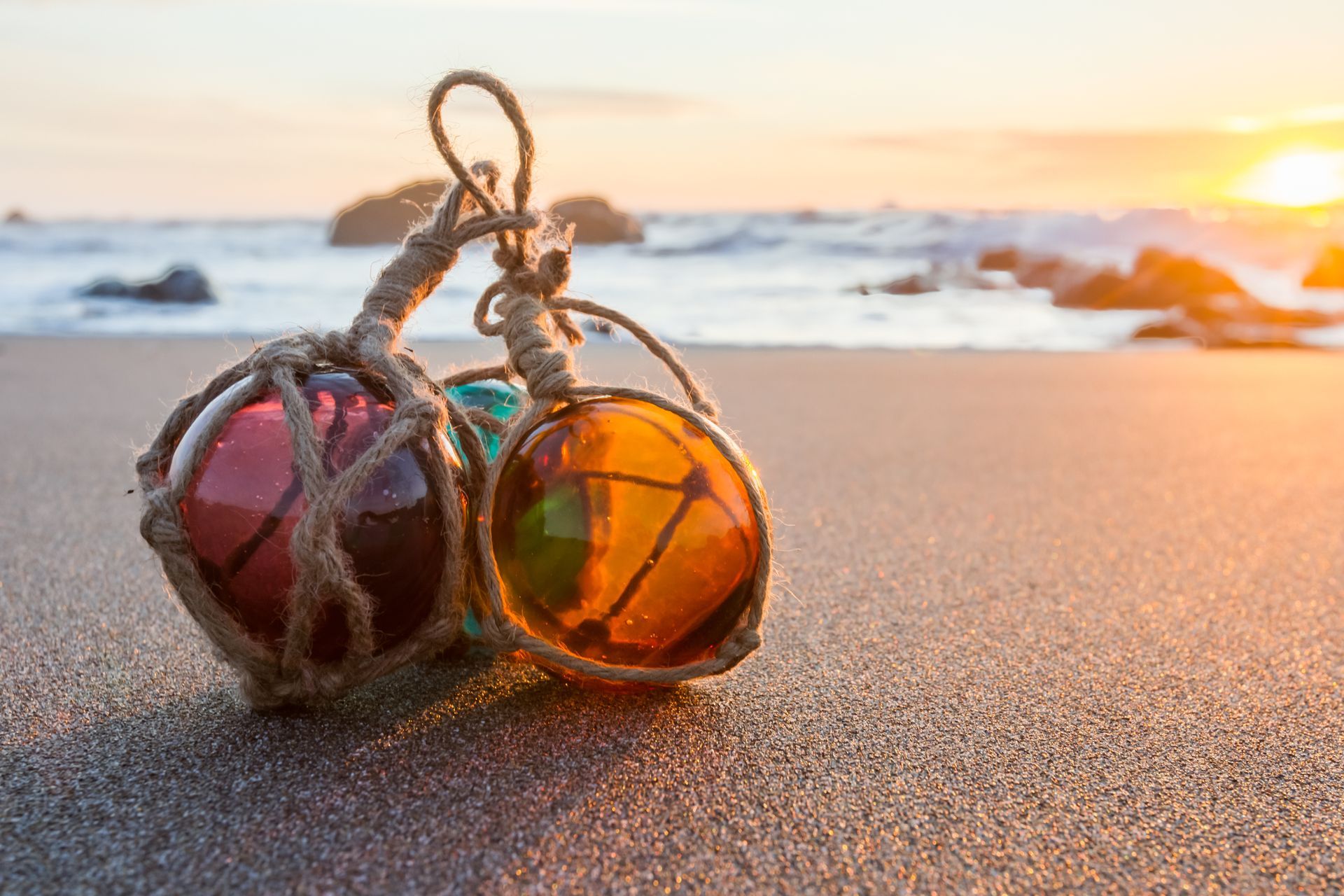 Two colorful glass fishing floats tied in rope on a sandy beach at sunset
